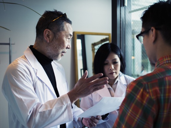 doctor giving notes to intern in front of patient